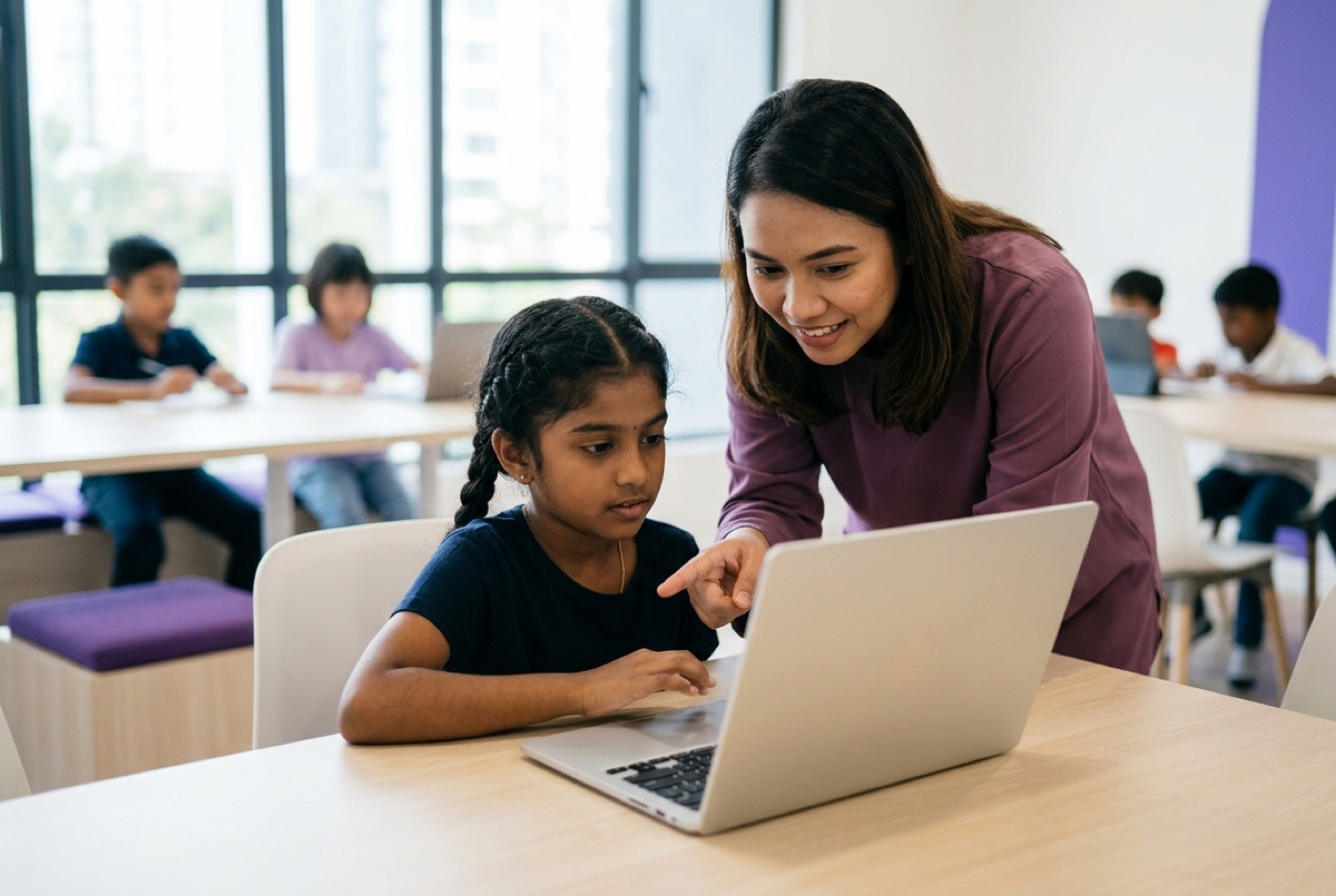 A supportive instructor guiding a young student working on a laptop in a brightly lit modern learning centre