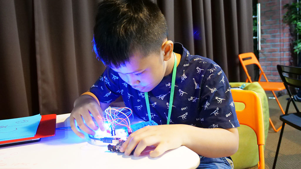 A young Kidocode student lighting up an Arduino circuit, focused on the build